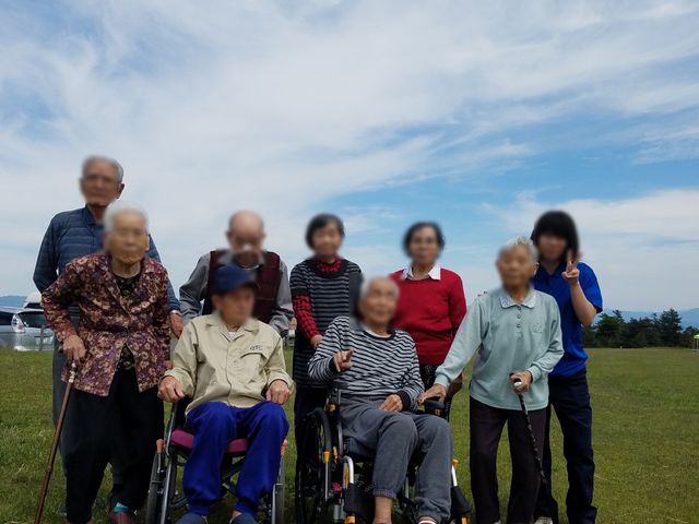 外で笑顔の集合 外出 青空の下、広々とした場所でリラックスする利用者様の姿です。様々なニーズに応える環境が整っています。