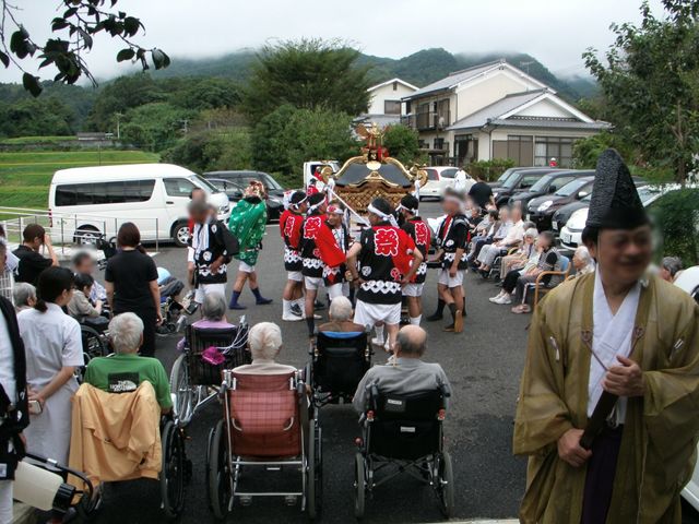 祭りを観る利用者とスタッフ 地域イベント 地域の祭りを施設の中庭で楽しむ利用者の方々。スタッフも一緒に和やかなひと時を過ごしています。