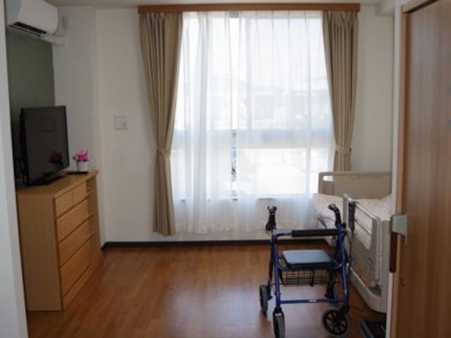 居室のきれいな空間 居室 床は清潔感のあるフローリングで、大きな窓からは自然光がたっぷりと入る明るい個室です。壁面の棚や家具は使いやすさを考慮して配置されており、快適な生活空間を提供しています。