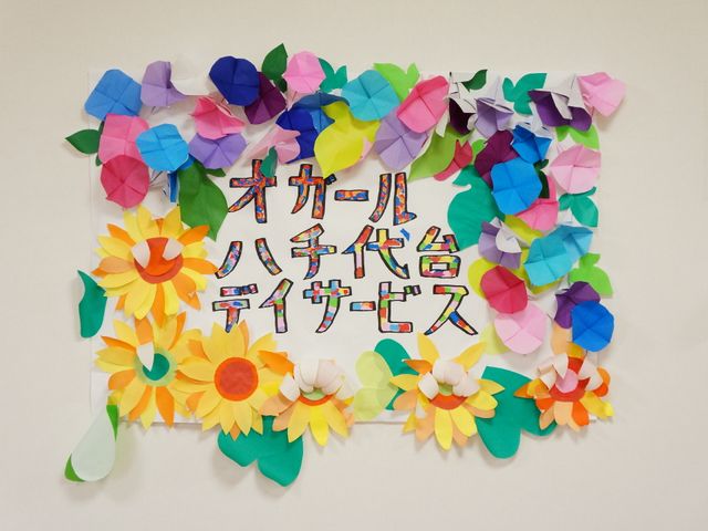 カラフルな壁飾り 作品 壁には手作りの花が飾られ、楽しい気持ちを演出しています。こちらでの就業は創造性を活かせる環境です。