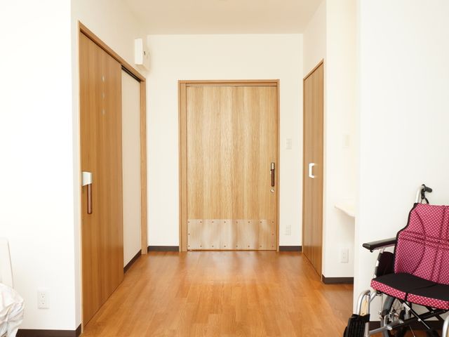 居室のドアと車椅子 居室 木目調の清潔感のあふれる居室です。車椅子のための十分な通路スペースが確保されており、快適な生活が送れる環境が整っています。