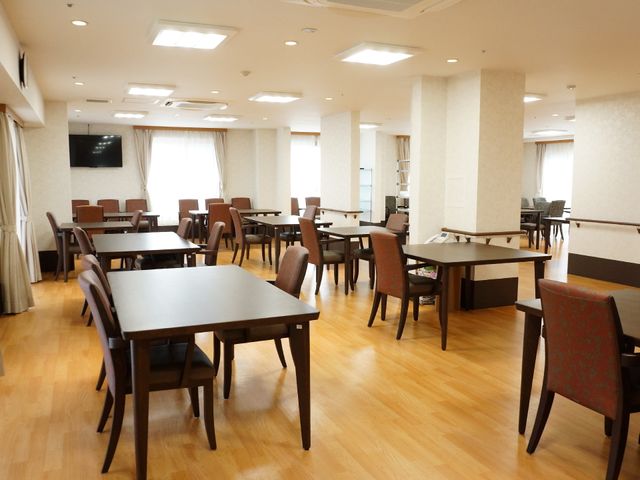 明るい食堂の空間 食堂 ゆったりと配置されたテーブルと椅子からは、開放的で落ち着いた雰囲気が感じられます。大画面のテレビがあり、共有スペースでのくつろぎのひとときを提供します。