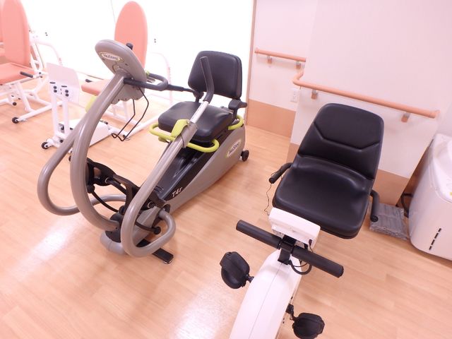 運動器具が置かれた部屋 バイク２種 設備の整った機能訓練室で、多様な運動器具を使用して身体機能の維持向上が図れます。明るく清潔な空間が確保されており、日々のトレーニングに最適です。