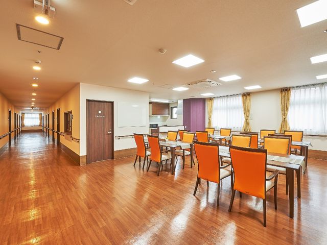 広々としたダイニングスペース 食堂・談話室 木目調の床が温かみを感じさせる食堂で、ゆったりとした時間を過ごすことができます。オレンジ色の椅子が明るい雰囲気を演出しています。