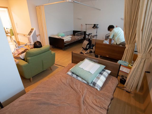 居室での生活風景 静養室 明るく広々とした居室で、スタッフが丁寧な対応をしています。この快適な環境で働くことができます。