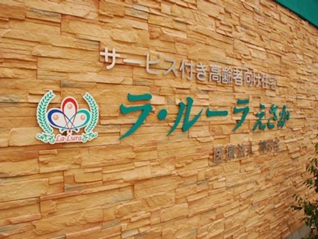 石壁に掲げられた施設看板 看板 心温まるデザインの看板が、あたたかな雰囲気を伝えており、訪れる方を温かく迎えてくれるでしょう。