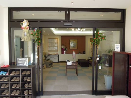 自動ドアの手前に、靴箱やスリッパの入った棚が設置されている。ドアの横にはしめ縄や花が飾られ、奥には鏡餅が置いてある。