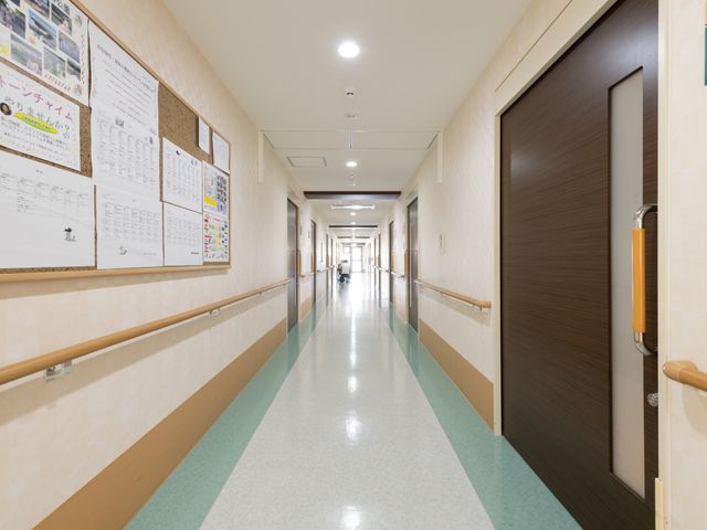 清潔感のある明るい廊下 通路 清潔で明るい廊下が広がっており、壁にはインフォメーションボードが掲示され、日々の生活に役立つ情報が満載です。先におられる方々は心地よい散策を楽しんでいらっしゃいます。