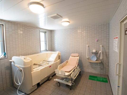 タイル張りの広々とした浴室に、入浴用のストレッチャーと機械浴槽が設置されており、壁にはシャワーが取りつけられている。
