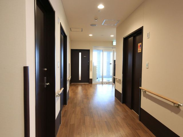 清潔な廊下の様子 通路 手すり沿いに続く明るい廊下は清潔感があり、落ち着いた木目調が心地よい空間を演出しています。安全で快適なケアのための環境が整っております。