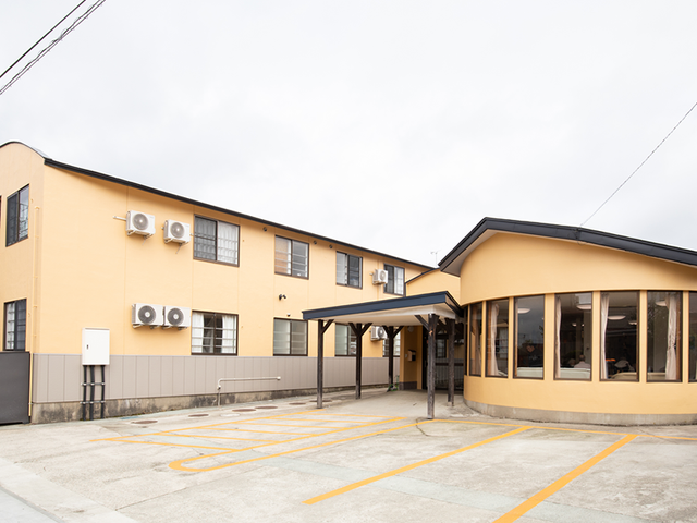 建物外観 外観   淡い色合いの建物で、玄関まで屋根付きの通路があります。駐車スペースも広く、雨の日の出入りに配慮されています。