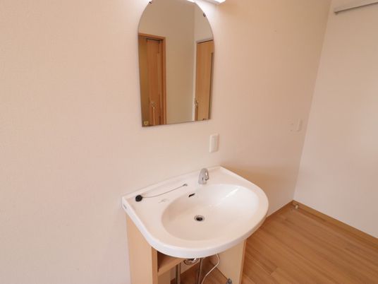 居室備え付けの洗面台。照明と共に壁に直接固定されている鏡は、上面が丸いカーブを描いたデザインになっている。