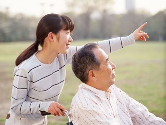 車椅子に乗った男性とそのご家族。車椅子を押しているご家族は笑顔で遠くを指差している。またその指差す方向を見つめる男性もほほ笑んでいる。