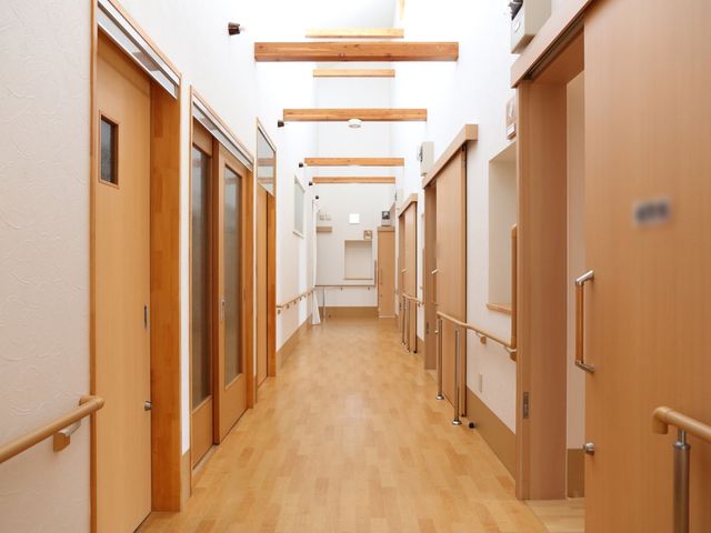 手すり付きの明るい廊下 通路 手すりが整備されており、歩行に不安がある方も安心してご利用いただける廊下です。木目調の扉と床が温かみのある雰囲気を演出しています。