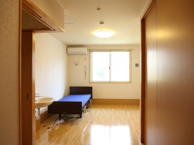 居室のベッドと洗面台 居室 落ち着いた色合いの居室です。日当たりが良く、必要な設備が整っておりますので、快適にお過ごしいただけます。