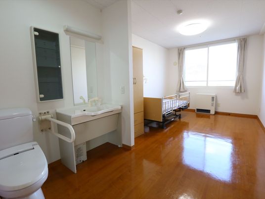 ピカピカに磨かれた床が光る、明るい雰囲気の部屋である。手すりが取りつけられたトイレの隣に洗面台が設置されている。