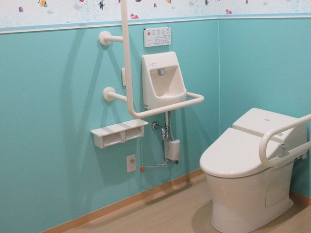バリアフリートイレ設備 トイレ 手すり付きのトイレで安全かつ快適なサポートを提供し、ご利用者の自立を促します。壁にはやさしい色彩と柄が施されており、明るい雰囲気を醸し出しています。