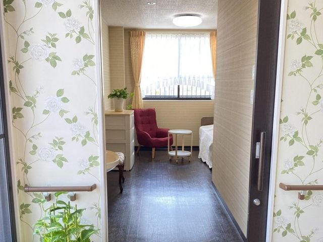 明るい居室 居室   花柄の壁紙が印象的な居室です。窓から光が入り、椅子と小さなテーブルでくつろぎやすい雰囲気です。