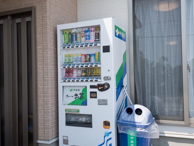 自動販売機とごみ箱外観 玄関前 休憩時に便利な自動販売機が設置されており、日々の息抜きに役立ちそうです。快適な職場環境を提供するこだわりが感じられます。