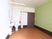 茶色い床と壁の１面が黄緑色のクロスが貼られている洋室の部屋である。トイレと洗面台があり、天井にカーテンレールが取りつけられている。