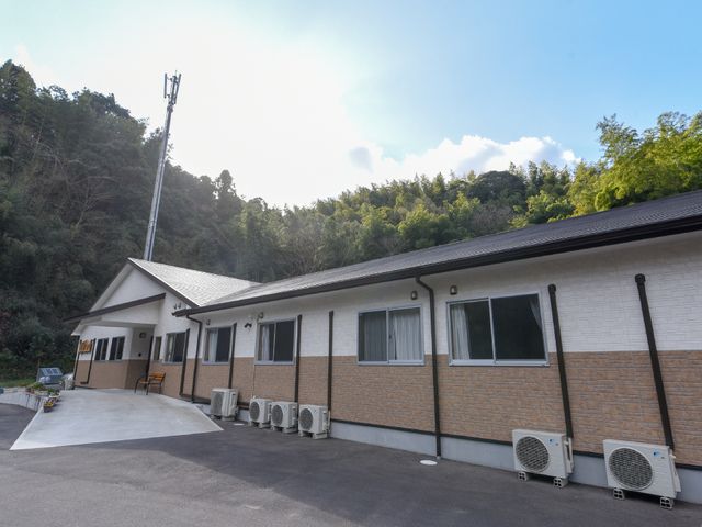 屋外の建物と自然の背景 外観 緑豊かな環境に佇む、清潔感のある一階建ての建物です。ゆとりを感じる空間で働くことができそうですね。
