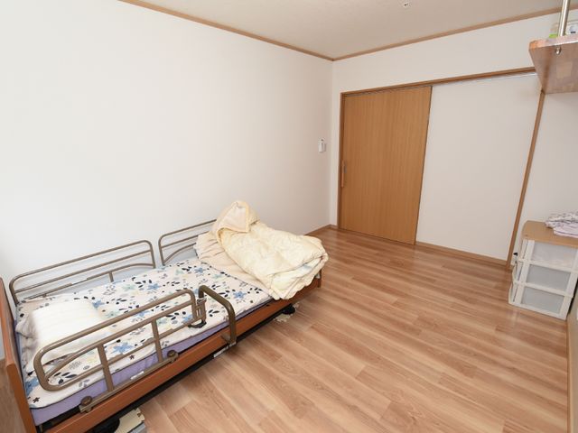 シンプルな居室の一角 居室 床のフローリングが美しい居室です。手すり付きのベッドが置かれ、静かで落ち着いた雰囲気が感じられます。