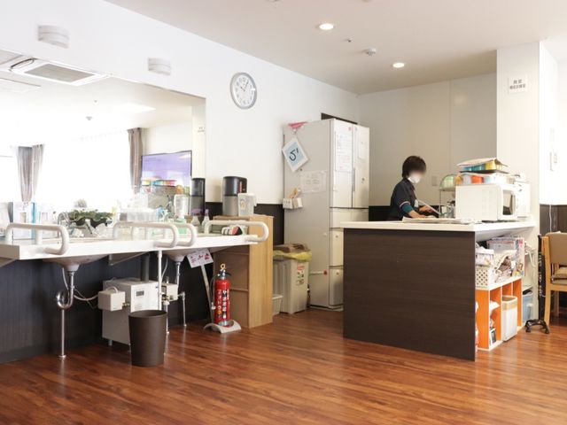 スタッフが作業するカウンター 食堂 温かみのある木目調の床と清潔感のあふれるカウンターで、スタッフが丁寧に業務をこなしています。コミュニケーションも円滑に行える開放的な空間が広がっております。