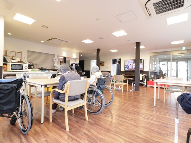 居室の日常風景 食堂 明るく広々とした食堂で、利用者の方がリラックスしながら過ごされています。テレビを見たり、会話を楽しんだりと、居心地の良い時間が流れています。