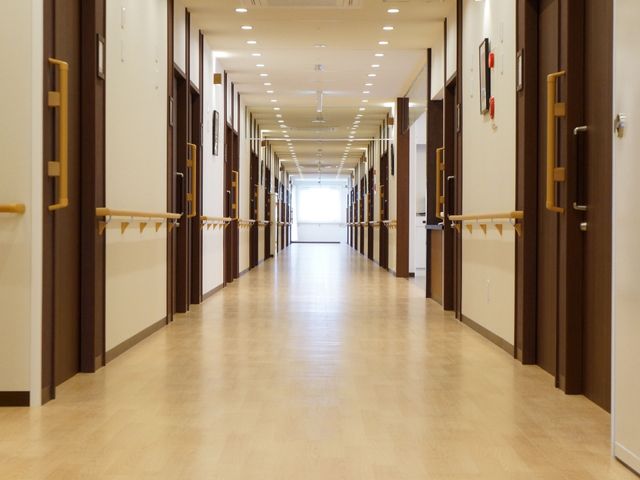廊下の清潔なイメージ 通路 手すり沿いに整然と並んだ扉が印象的な廊下です。明るく広々としており、ご高齢の方でも安心して歩ける設計になっています。