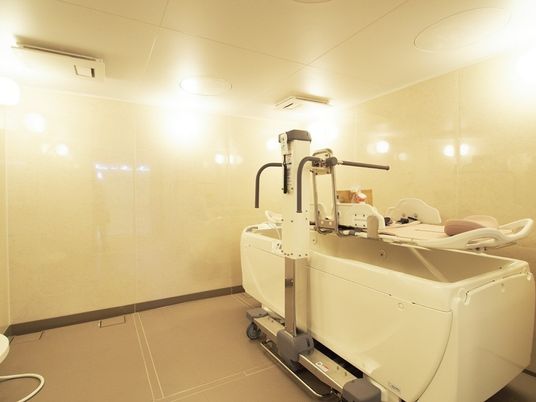 施設の写真 介助スタッフが一緒に入室できる広い浴室内に、寝たまま入浴可能な介護入浴機器が設置されている。浴室暖房が付いている。