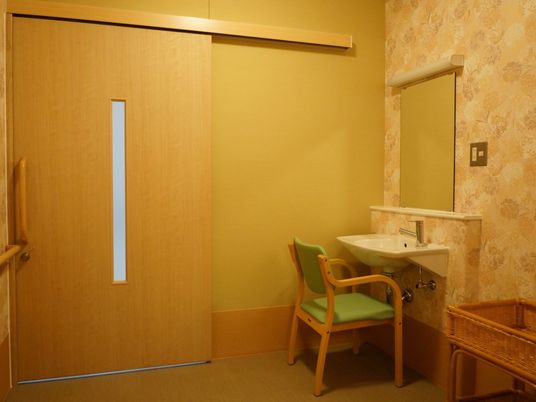 施設の写真 花柄の壁紙が貼られた個室。鏡付きの洗面台が設置されており、横には着替えを入れるためのカゴが置かれている。