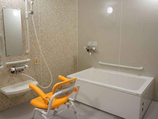 施設の写真 手すりが設けてある。大きめの１人用の浴槽。介護用の椅子が置かれている。ナースコールが設置されており、いざと言うときも安心。