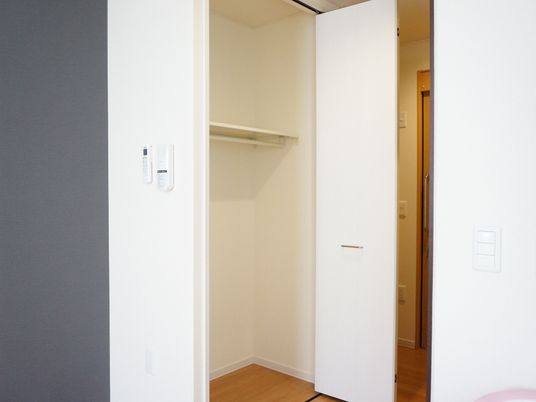 居室には折れ戸扉の収納スペースがある。棚が１段作りつけられ、ハンガーラックが設置されている。壁には室内照明のスイッチがある。