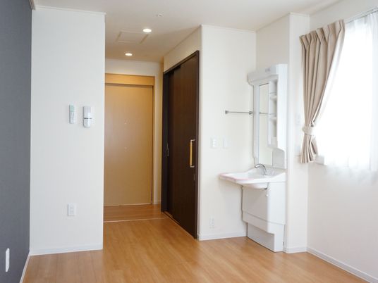 居室に入るとトイレと収納スペースが向かい合わせになっている。トイレ横は洗面台になっている。壁にタオル掛けが設置されている。