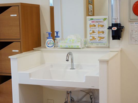 洗面台の壁には紙コップホルダーが設置されている。正しい手洗いの仕方のイラストが貼られ、ハンドソープが置かれている。