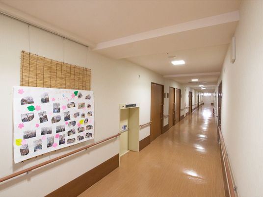 施設の写真 白とブラウンを基調とした廊下スペースは、行き届いた清掃でスッキリとした空間である。壁に思い出の写真のレイアウトを取り入れている。
