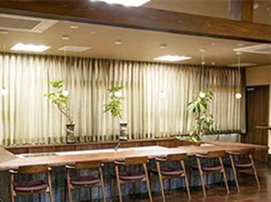 施設の写真 カウンター状のテーブルに沿って６脚の椅子が並んでいる共用空間である。テーブルの奥には３鉢の観葉植物が置かれている。