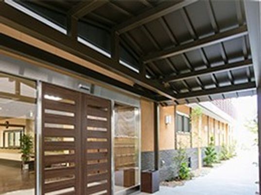 施設の写真 エントランス外側は、内側が濃い茶色に塗装された三角屋根が玄関上にせり出す、伝統的な和風建築の流れを感じさせる造りとなっている。