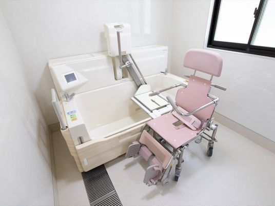 施設の写真 小窓が設置された浴室で、日中は日差しがはいる。ピンク色の専用搬送車、白色の介護浴槽が備え付けられている。