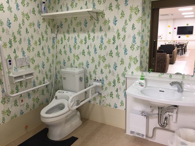 バリアフリートイレと洗面台 トイレ サポートバー付きのトイレと広々とした洗面台が設置され、安心してご利用いただける空間です。隣接する共用スペースも明るく開放的な雰囲気が漂います。