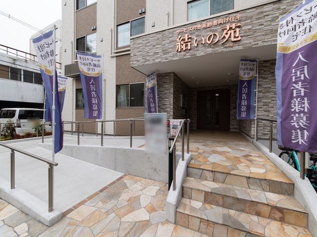 入口と看板が印象的な建物 エントランス スロープと階段の両方が備わり、バリアフリーに配慮された建物の入り口です。歓迎する雰囲気の看板が目に優しい印象を与えています。