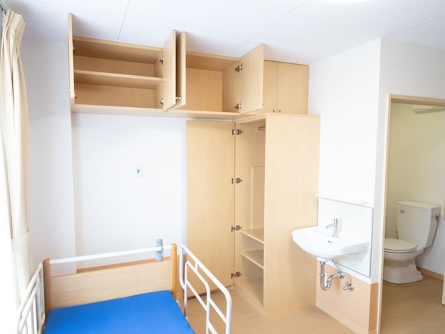居室のベッドと収納 居室 広々とした居室には、収納も豊富で日々の生活に必要なものを整理しやすいデザインです。ベッド横には手洗い場があり、衛生的に過ごせます。