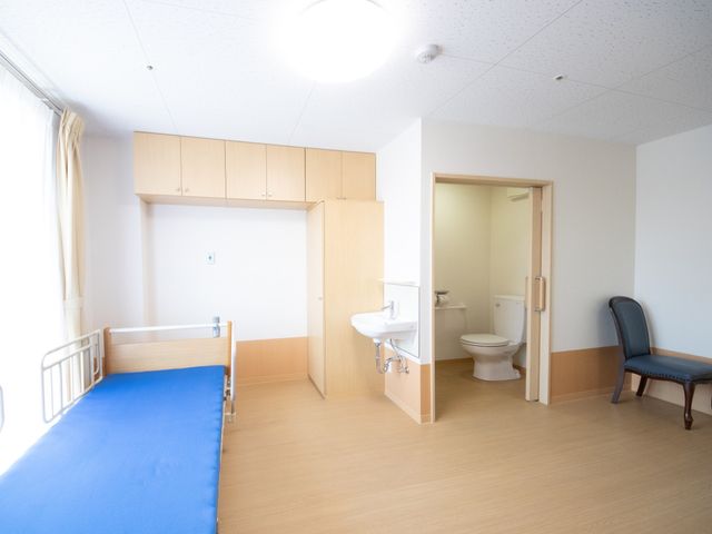 居室のベッドとトイレ 居室 広々とした清潔感のある居室です。個別の洗面台とトイレが完備され、プライバシーと快適さを重視した空間となっています。