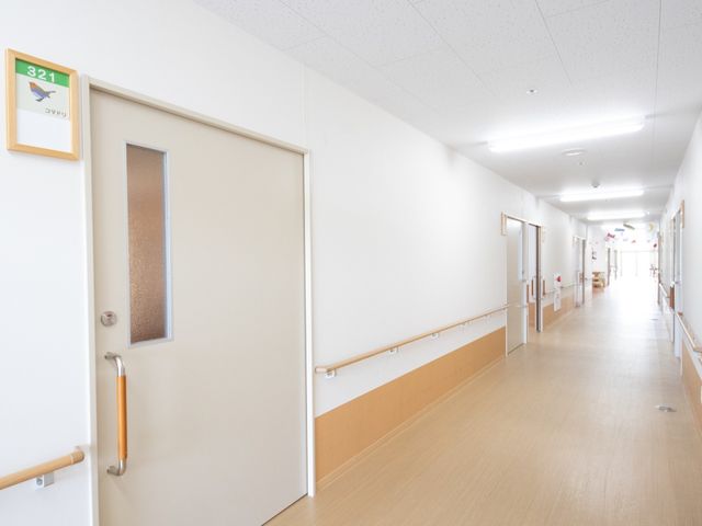 明るい廊下と部屋の入口 通路 手すりが設置された安全に配慮した廊下です。職員や利用者の方々が快適に過ごせるよう、ゆったりとした通路を確保しています。
