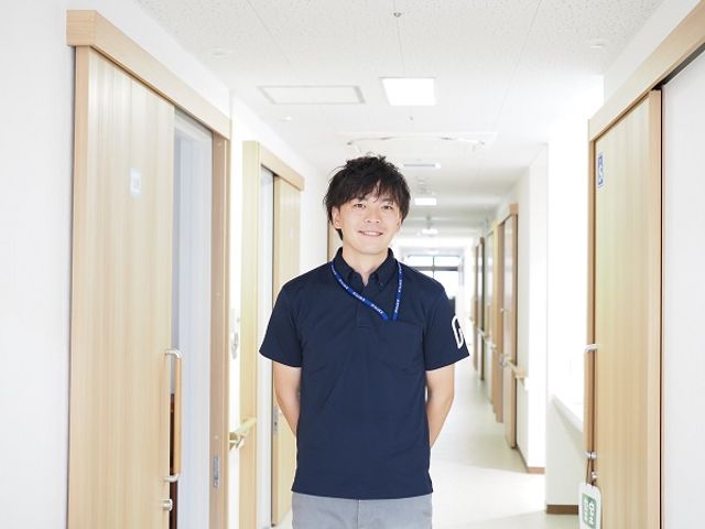 廊下で立つスタッフ 笑顔で立つスタッフが、清潔感あふれる廊下で皆さんをお迎えします。働く環境の良さが感じられる明るい場所です。