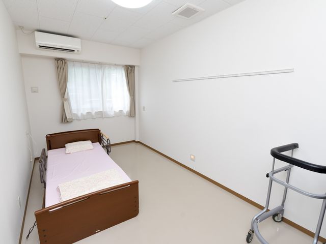 清潔な個室の居室 居室 広々とした居室には、ベッドと歩行補助の手押し車が見受けられ、日差しの優しい窓辺が印象的です。落ち着いた空間で、快適な日々を送ることができそうです。