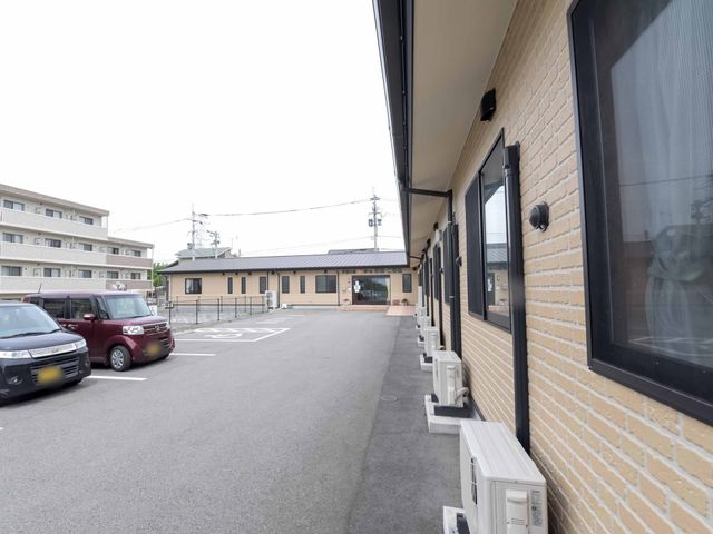 敷地内の駐車場と建物外観 外観 広々とした駐車スペースがあり、出勤時の利便性が考慮されています。明るい色合いの建物は、訪れる際の印象を和やかにしてくれます。