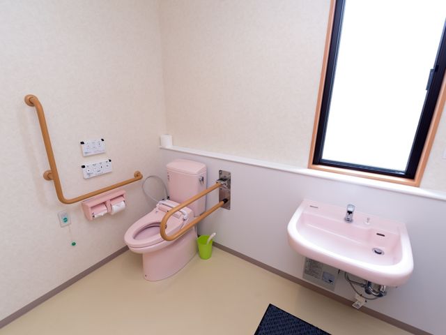 バリアフリーの洗面所とトイレ トイレ すべての方が安心してご使用いただけるよう、手すりが完備された広々としたトイレです。窓からの自然光が心地よい清潔感ある空間を演出しています。