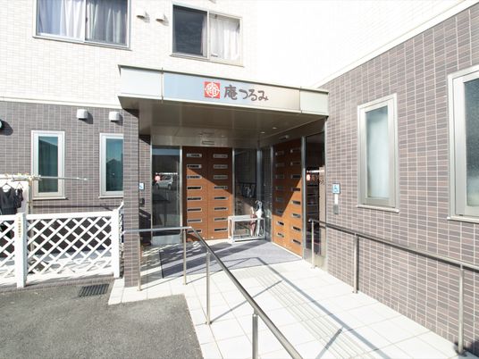 玄関前には茶色い両開きの扉が正面と右側にある。舗装された通路の両側には長い手すりが取りつけられている。