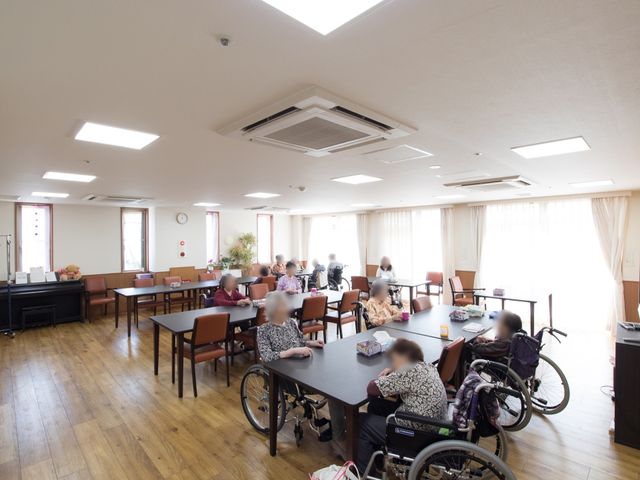 居室内にいる人々 食堂 広々とした食堂で、利用者がくつろぐ姿が見受けられます。テーブルを囲んだ椅子は、皆さんの交流の場ともなっているようです。